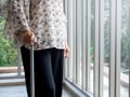 Close up senior woman`s hand holding a walking cane standing alone near the glass window. Royalty Free Stock Photo