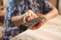 Close up of senior woman sitting on chair near the desk and holding tv remote control. Selective focus. Royalty Free Stock Photo