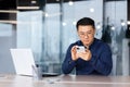 Close-up of serious and pensive Asian businessman using phone, man inside office typing message, browsing internet pages Royalty Free Stock Photo