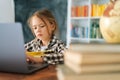 Close-up of serious unhappy elementary child school girl doing writing homework holding pen sitting at table with laptop Royalty Free Stock Photo