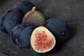 Close up of several dark figs lying on an old metal plate. A fig is cut open