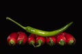 Close up of several red chillies lying side by side. A green pod lies on top of the red pods. The background is dark