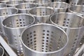 Close up of several rows of metal containers with holes on a shelf in a store or on a production line in a factory