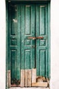 Close-up of shabby green wooden doors locked with a broken bottom and planks at the entrance. Royalty Free Stock Photo