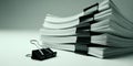 Stack of white paper documents held together by black binder clips on a light grey surface with a single binder clip Royalty Free Stock Photo