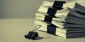 Pile of white paper documents bound by black binder clips on a muted beige surface with a single binder clip in the Royalty Free Stock Photo
