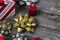 Close up of a shiny gold bow with gift boxes and burning candles in background on rustic wooden planks for a merry Christmas or Royalty Free Stock Photo