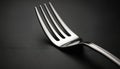Close up shiny silver fork with four tines on a dark textured background. It is a single utensil ready for a meal. This image is Royalty Free Stock Photo