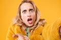 Close up of shocked perplexed young blonde woman in yellow fur coat posing isolated on orange background in studio