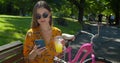 Close-up shooting. Portrait of attractive young woman with a bicycle used smartphone and drinking lemonade on a park Royalty Free Stock Photo