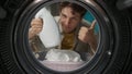 View from inside the washing machine, adult man with laundry basket holding a bottle of softener in hand Royalty Free Stock Photo