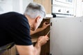 Close up shot of aged repairman in uniform working, fixing kitchen cabinet using screwdriver. Repair service concept