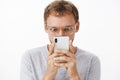 Close-up shot of amused and entertained male geek in glasses holding smartphone close to face popping eyes and staring Royalty Free Stock Photo