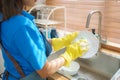 Close-up shot of Asian woman housewife washing dishes in a sink wearing rubber gloves in the kitchen of the house Royalty Free Stock Photo