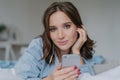 Close up shot of attractive brunette young woman downloads songs from network, uses smart phone for entertainment, dressed in nigh