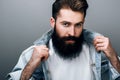 Close up shot of attractive brutal fashionable young European male with thick beard wearing trendy denim jacket, staring at camera