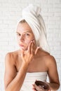 Preoccupied young woman in white bath towels applying scrub on her face