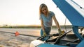 Close up shot of attractive young woman looking under the hood of her broken car, trying to repair it on her own while Royalty Free Stock Photo