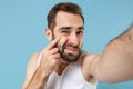 Close up shot bearded young man 20s years old in white shirt doing selfie isolated on blue pastel wall background