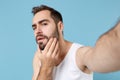 Close up shot bearded young man 20s years old in white shirt doing selfie isolated on blue pastel wall background