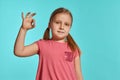 Close-up shot of beautiful blonde little girl in a pink dress posing against a blue background. Royalty Free Stock Photo