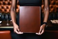 Close-up shot of a black waitress hands holding a blank brown leather-bound menu facing towards the camera Royalty Free Stock Photo
