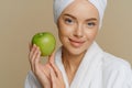 Blue eyed woman with minimal makeup well cared complexion fresh clean skin dressed in white coat holds green apple Royalty Free Stock Photo