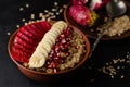 Close up shot of a bowl with oat porridge, banana, pomegranate seeds and opuntia cactus fruit on black background