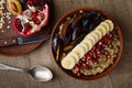 Close up shot of a bowl with oat porridge, banana, pomegranate seeds and plum on sackcloth background. Overhead, flat lay