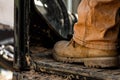 Close-up shot of brown leather boot of a construction worker sitting on an aged dirty tractor Royalty Free Stock Photo