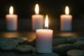 Close-up shot of a burning candle on flat stones with the background of three blurred candles