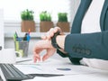 Close up shot of a business woman checking time on her smartwatch. Female sitting in office with a laptop and cup of Royalty Free Stock Photo