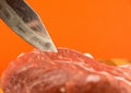 Close-up shot of a butcher`s knife and a piece of red raw pork meat on a bright orange background. Butcher`s shop. Meat cutting Royalty Free Stock Photo