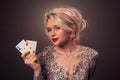 Blonde woman with a beautiful hairstyle and perfect make-up is posing with playing cards in her hands. Casino, poker. Royalty Free Stock Photo