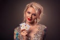 Blonde woman with a beautiful hairstyle and perfect make-up is posing with playing cards in her hands. Casino, poker. Royalty Free Stock Photo