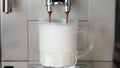 Close up shot of coffee pouring into glass cup with milk, making cappuccino using the automatic coffee machine. Beverage Royalty Free Stock Photo