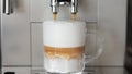 Close up shot of coffee pouring into glass cup with milk, making cappuccino using the automatic coffee machine. Beverage Royalty Free Stock Photo