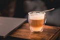 Close-up shot of a cup of Latte coffee with layers and frothy milk on a wood table with laptop