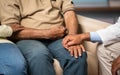 Close up shot of doctor and wife consoling senior elderly man by holding hands, while sitting on sofa at home - concept Royalty Free Stock Photo