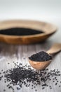 Close up shot of dried seeds of black cumin seeds kalinji on wooden spoon with wooden plate on background. Soft focus