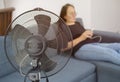 Closeup of black electric fan heater on floor in living room, with woman on couch in background Royalty Free Stock Photo