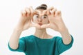 Close-up shot of emotive cute caucasian woman in glasses, pulling hands towards camera and zoom on heart gesture, gazing