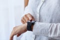 Close up shot of faceless woman in white clothing girl using her her smartwatch, touching touch screen while posing near window Royalty Free Stock Photo