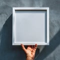 Hand Holding Blank White Square Frame Against Textured Gray Wall Royalty Free Stock Photo