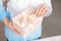 Close-up shot of female hands holding a small gift wrapped with pink ribbon. Small gift in the hands of a woman indoor Royalty Free Stock Photo