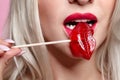 Portrait of blonde woman bites a lollipop. Red female lips shape lollipop. Sweet tooth concept