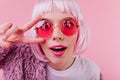 Close-up shot of funny european girl in colorful periwig and pink sunglasses. Indoor photo of attra