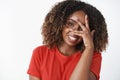 Close-up shot of funny tender and feminine dark-skinned woman with curly haircut close half of face with hand and Royalty Free Stock Photo