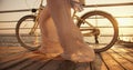 Close-up shot of a girl in a long white light dress who wriggles in the wind and walks near her bicycle along the beach