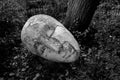 Close-up shot of a grayscale carved mask sculpture on a park floor